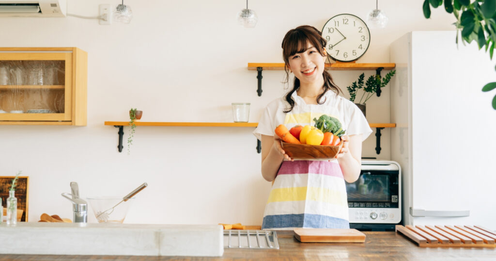 A woman is standing in the kitchen with vegetables